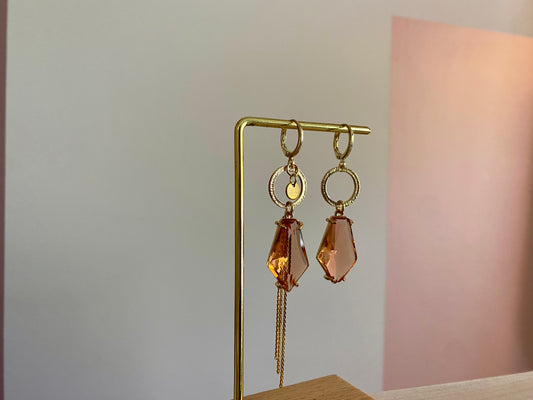 Asymmetrische oorbellen met gehamerde gouden ring, klein merk logo, roest oranje glasbedel in de vorm van een hexagon en gouden streng