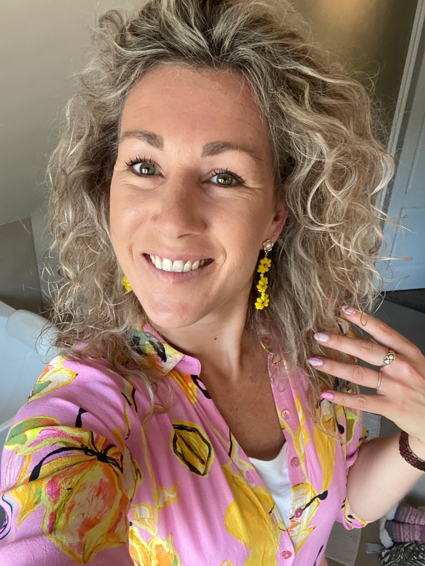 Model met Handgemaakte oorbel met 3 gele bloemen onder elkaar van glanzende kralen en een 14K vergulde steker met parel in de vorm van een bloem.