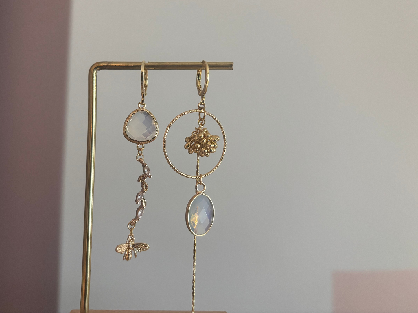 Asymmetrische 14k vergulde oorbellen met opaalkleurige natuursteentjes, bijtje met zirkonia en trosje, circa 6 cm lang.