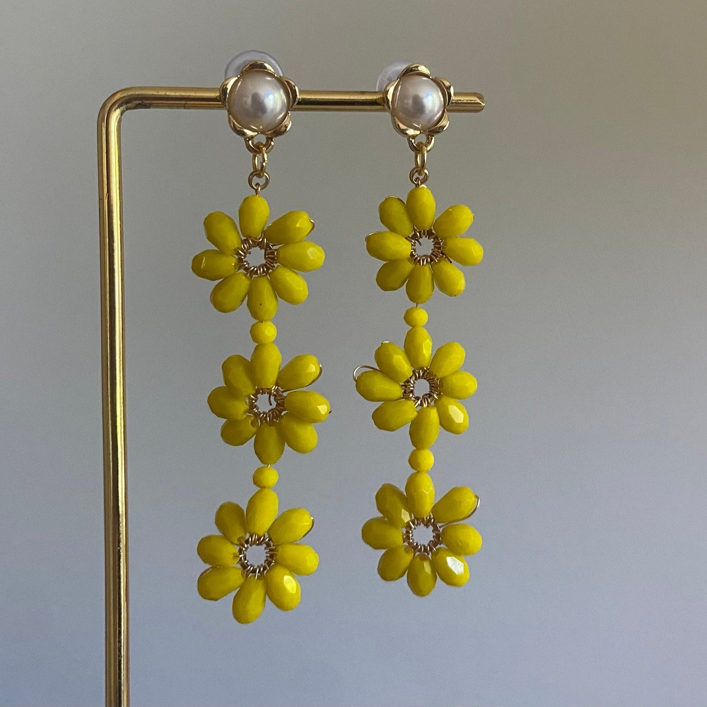 Handgemaakte oorbel met 3 gele bloemen onder elkaar van glanzende kralen en een 14K vergulde steker met parel in de vorm van een bloem.
