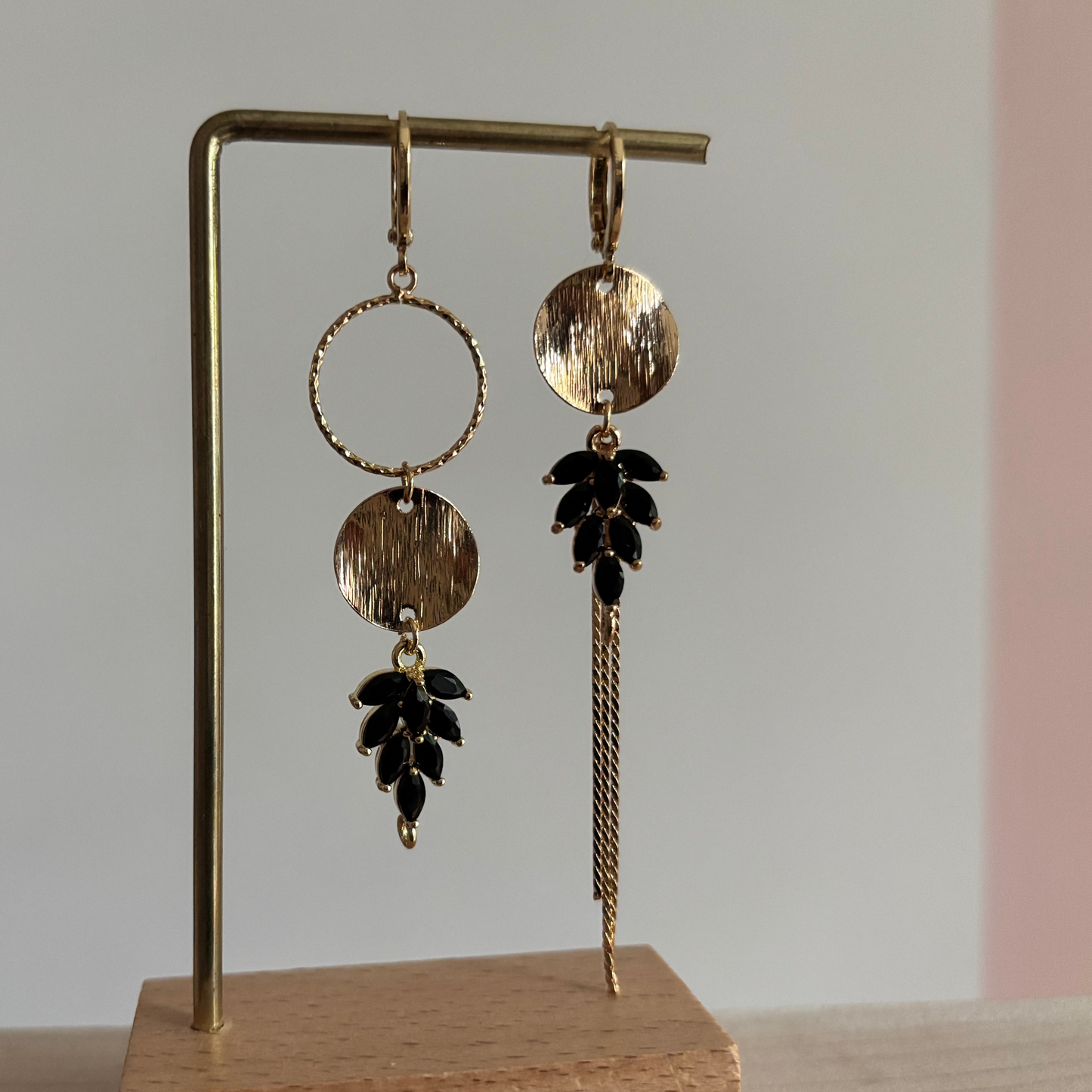 Gouden asymmetrische oorbellen Fabienne met schwarze steentjes op een standaard.