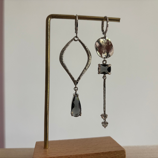 Zilverkleurige asymmetrische oorbellen Floor Zilver met een grote open ruit met grijze druppel en een strakke hanger met schijfje en zirkonia.