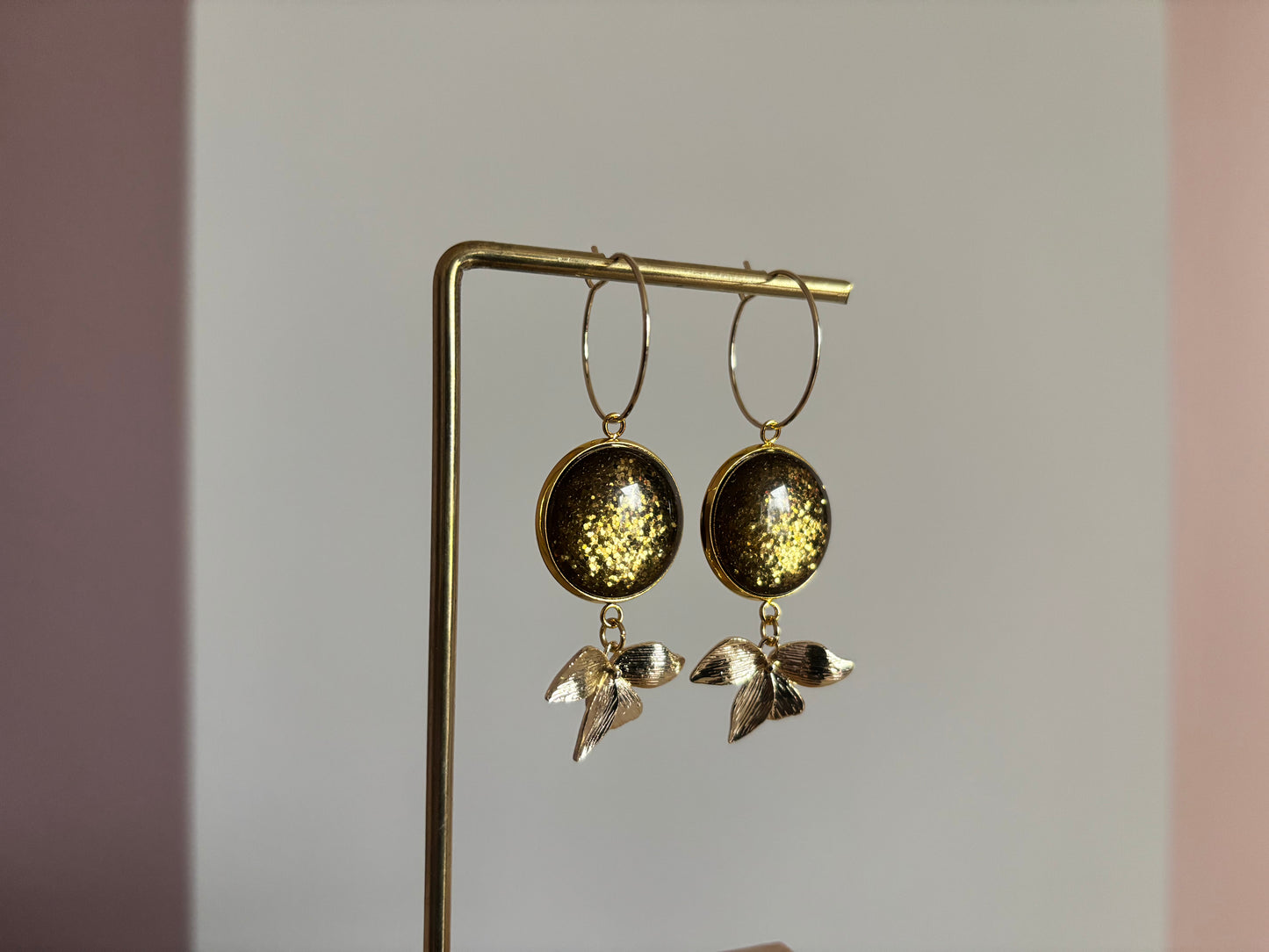 Gouden oorbellen met een 14k vergulde ring, een klein bladaccent en een ronde, groene glitter cabochon tegen een lichte achtergrond.