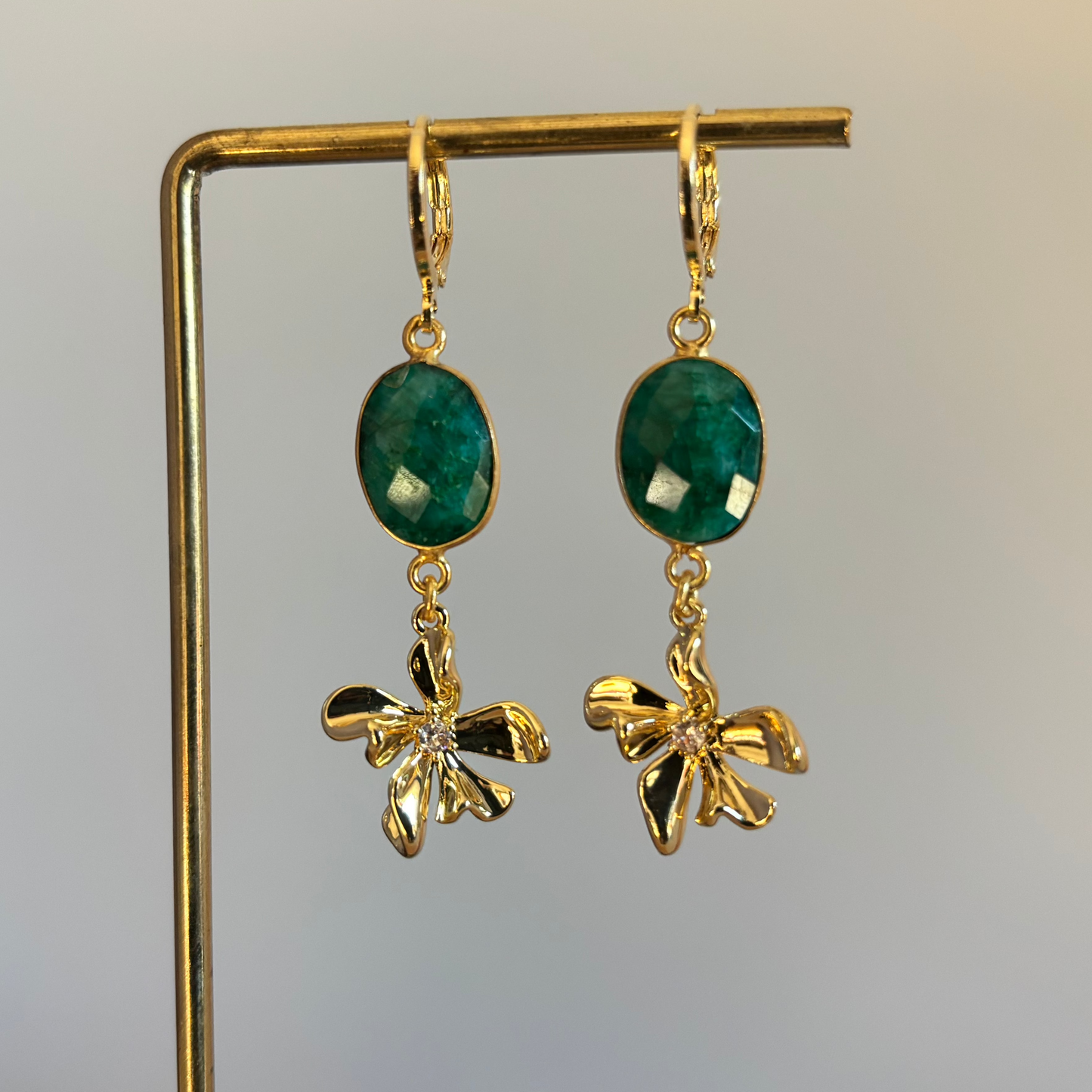 Gouden oorbellen met een diepgroene ovale steen en een goudkleurige hanger in de vorm van een bloem met een klein glimmend steentje in het midden."