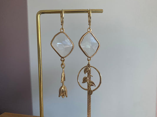 asymmetrisch paar oorbellen, twee verschillende oorbellen. Éen met een 14k vergulde roos andere met een bedel met bladeren ook 14k. Doorzichtige glazen bedel erboven