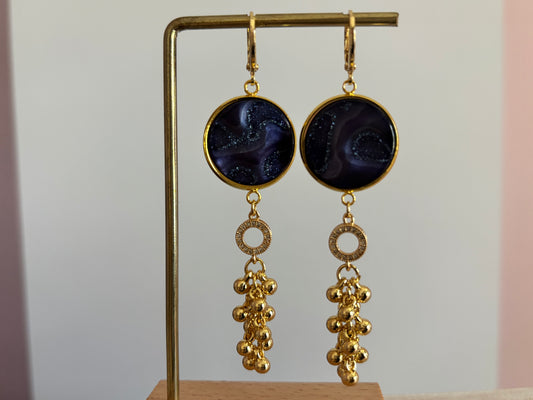 Goudkleurige oorbellen Joke met een donkerblauwe glinsterende polaris steen, strass-ringetje en goudkleurig bollentrosje