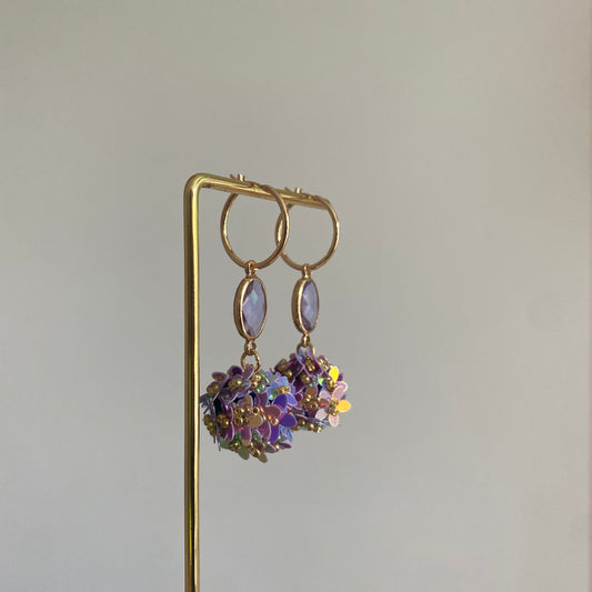 Bolletjes oorbel van holografische bloemetjes in zachtroze kleuren, een lila ovalen glasbedel en RVS oorringen