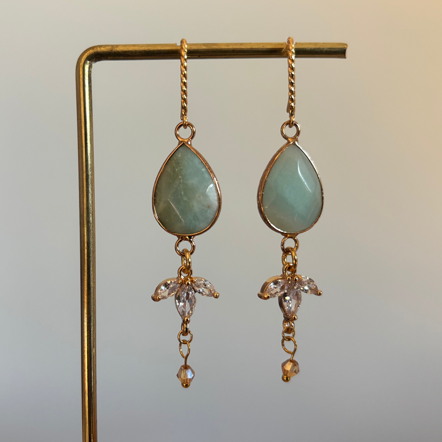 "Gouden oorbellen met een aventurijn mintgroen, een trio van heldere kristallen en een klein beige kraaltje."