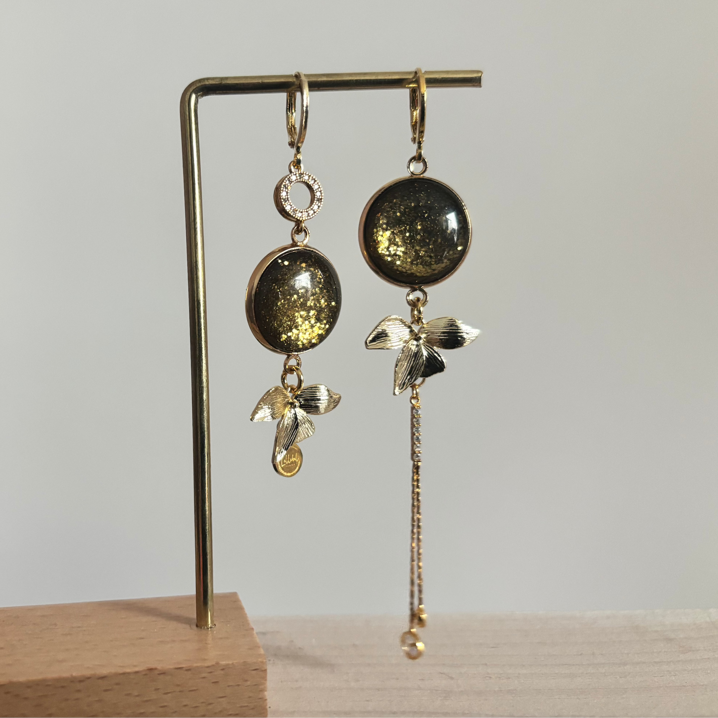 Vergulde asymmetrische oorbellen Olivia met donkergroene stenen en hangers in de vorm van blaadjes.