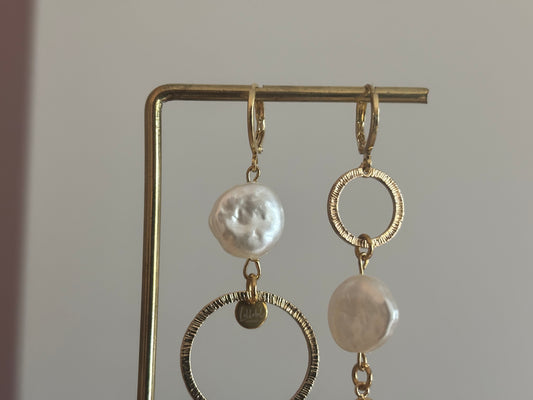 Asymmetrische oorbellen met gehamerde ringen, parel en schelp, circa 6 cm lang.