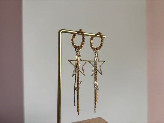 14k vergulde oorbellen 'Sterre' van Lellebel op een standaard. De oorbellen hebben een goudkleurige ster met daaraan hangende fijne kettinkjes en kleine glanzende zirkonia steentjes.