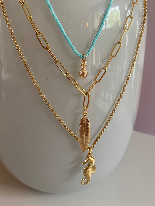 Vergulde 3 delige-RVS kettingen waaraan een een 14K verguld zeepaardje, veertje en een ananas hangen.