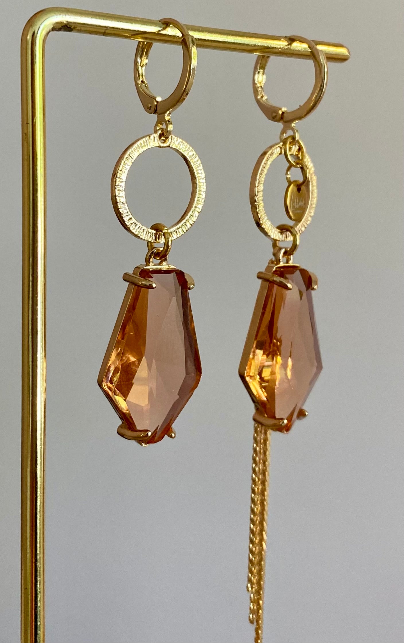 Asymmetrische oorbellen met gehamerde gouden ring, klein merk logo, roest oranje glasbedel in de vorm van een hexagon en gouden streng 