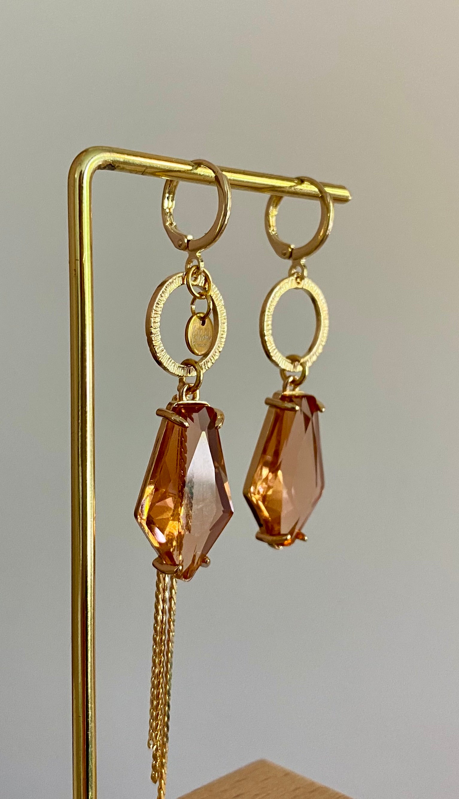 Asymmetrische oorbellen met gehamerde gouden ring, klein merk logo, roest oranje glasbedel in de vorm van een hexagon en gouden streng 