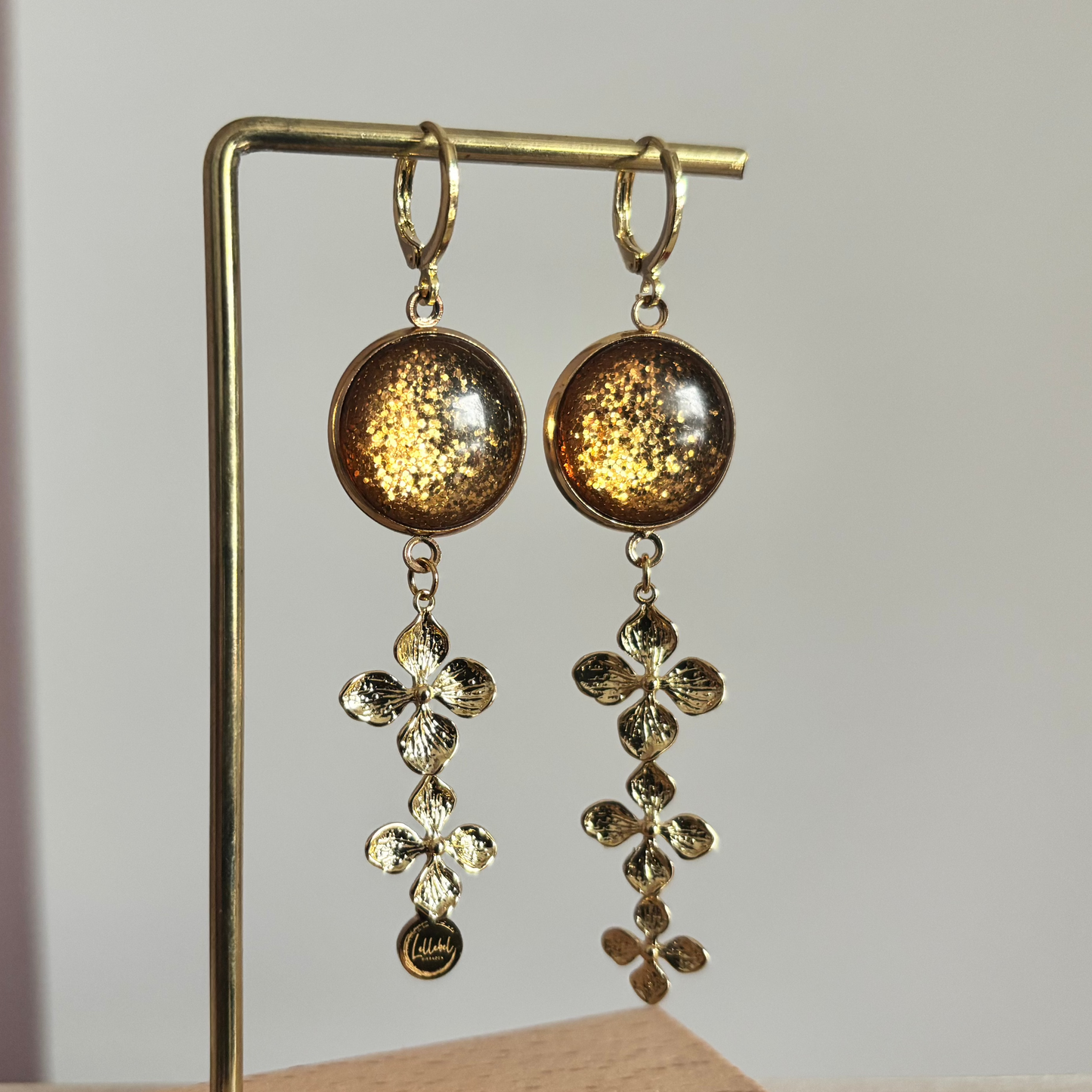 14k vergulde oorbellen 'Amber' met warmbruine glitterstenen en hangers van drie gouden bloemetjes.