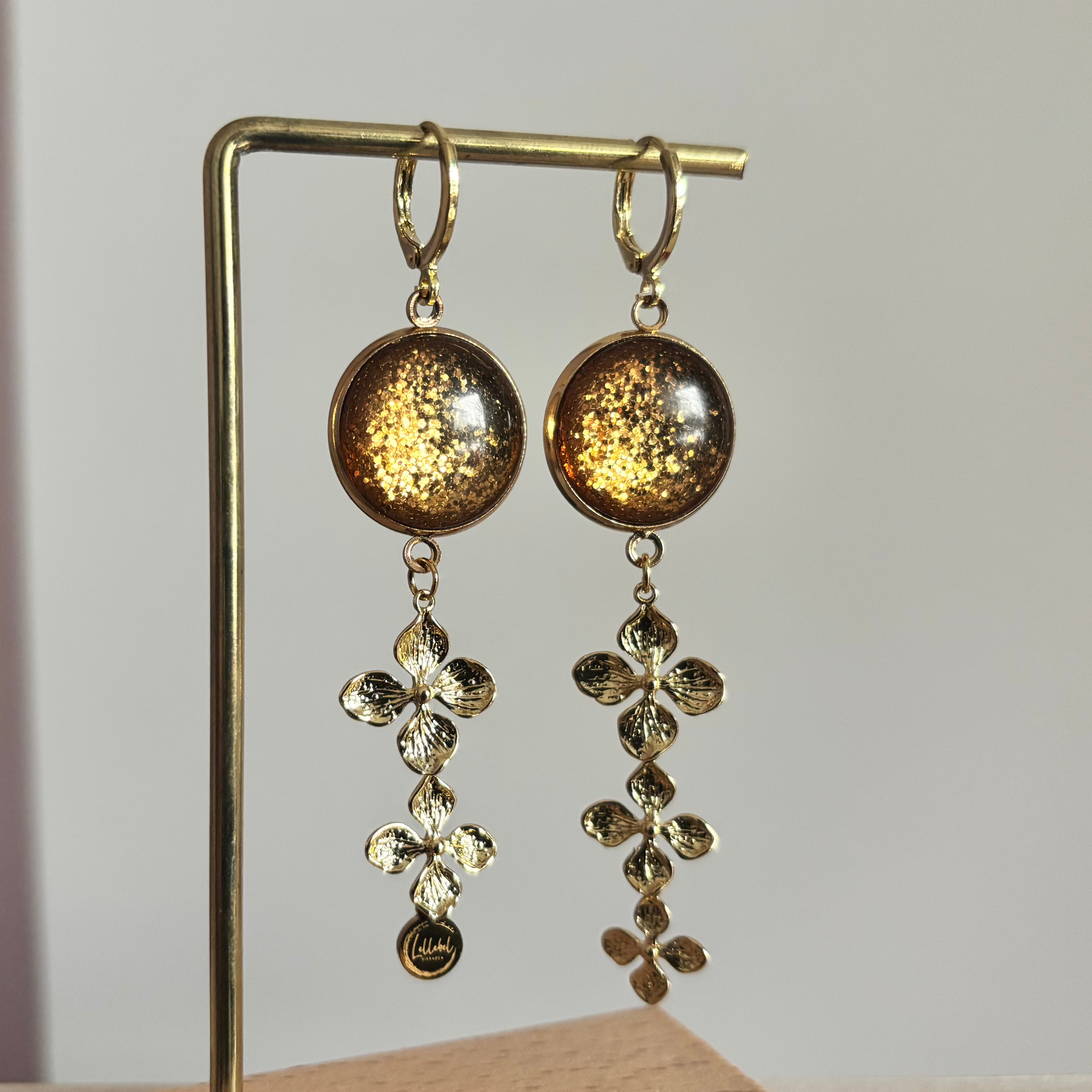 14k vergulde oorbellen 'Amber' met warmbruine glitterstenen en hangers van drie gouden bloemetjes.