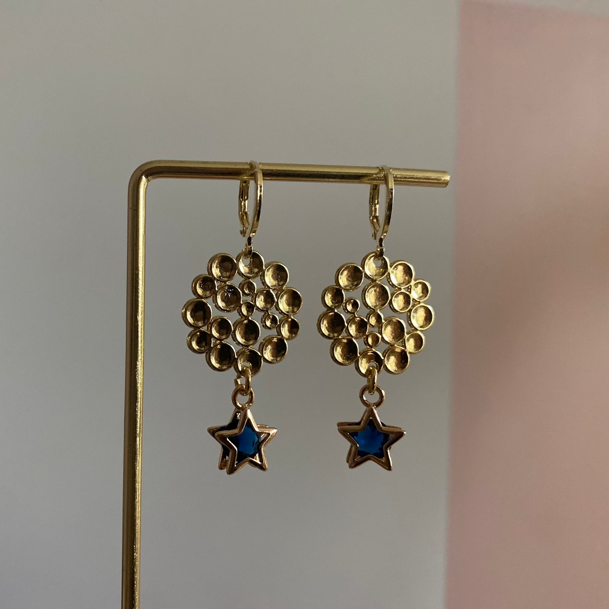 Een foto van de oorbellen "Annabelle"; Een 14k vergulde oorbel met ster en steentje, gecombineerd met een bubbelende hanger, lengte 4 cm.
