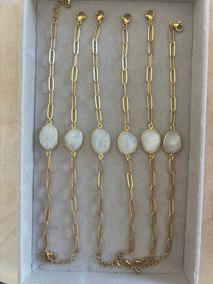 Zes goudkleurige Ada schakelarmbanden op een rij in een grijs sieradendoosje, elk voorzien van een grove langwerpige schakelketting en een centrale, ovale halfedelsteen met een wit-grijze glans.