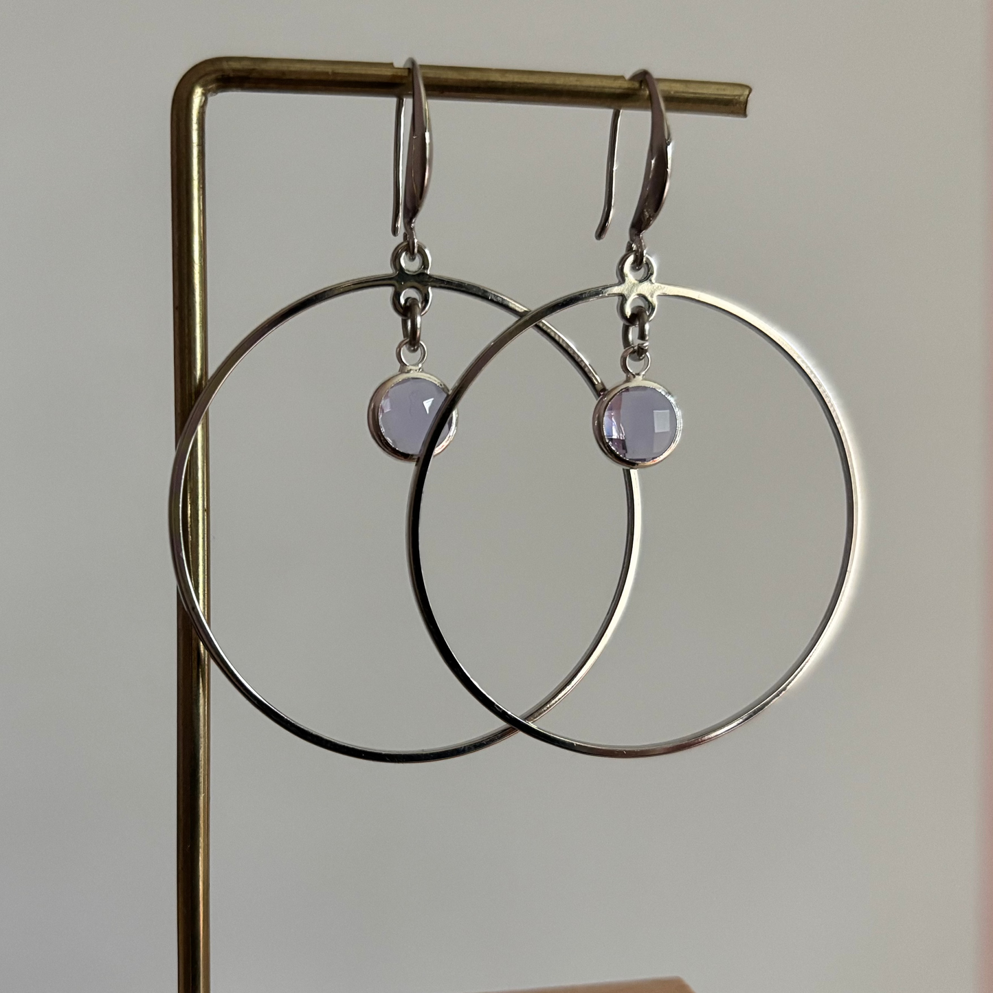 Zilverkleurige hangoorbellen bestaande uit een grote ronde ring van 40 mm met een lichtpaars kristal in het midden.