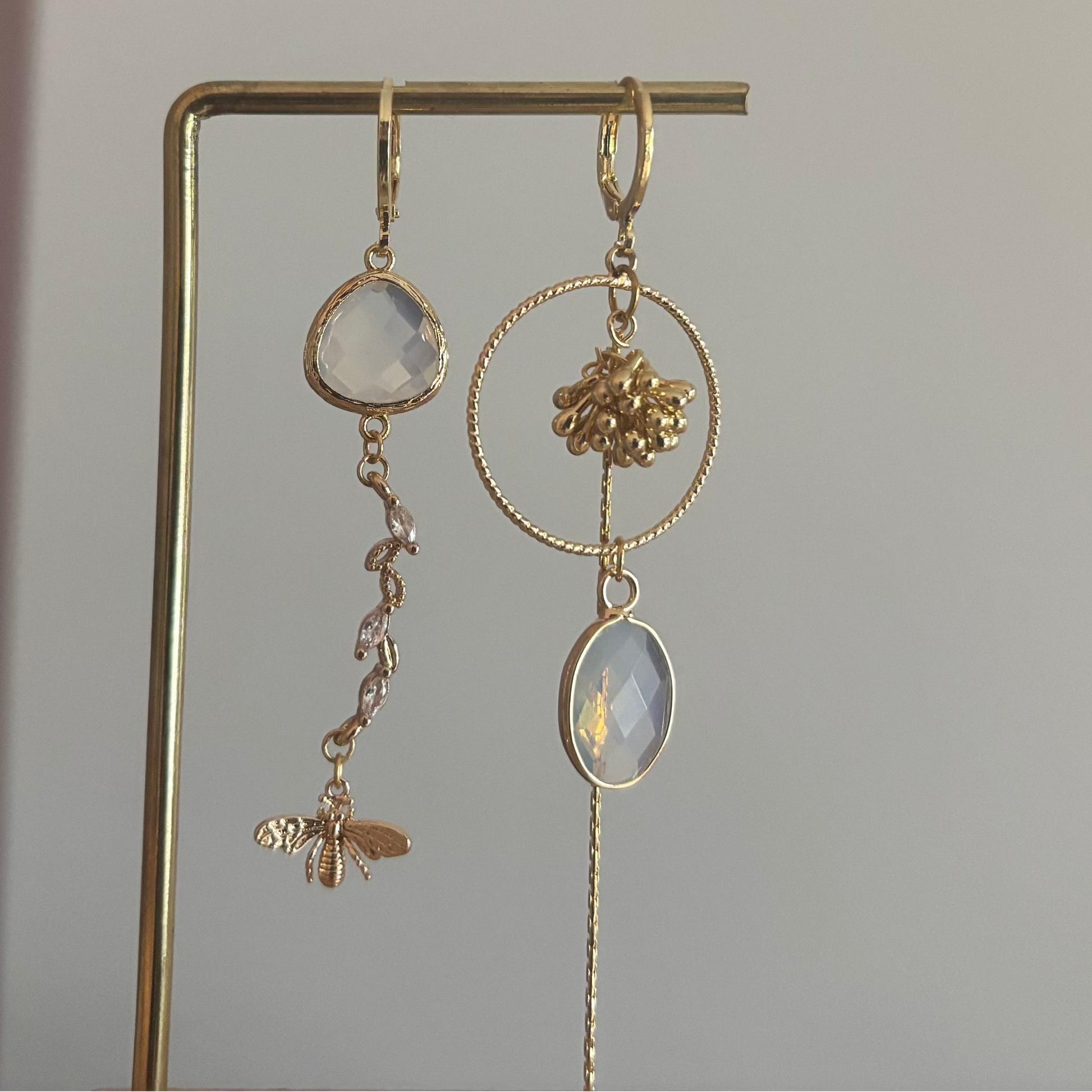 Asymmetrische 14k vergulde oorbellen met opaal­kleurige natuursteentjes, bijtje met zirkonia en trosje, circa 6 cm lang.