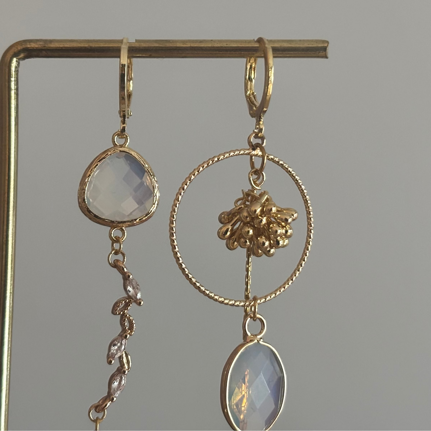 Asymmetrische 14k vergulde oorbellen met opaal­kleurige natuursteentjes, bijtje met zirkonia en trosje, circa 6 cm lang.