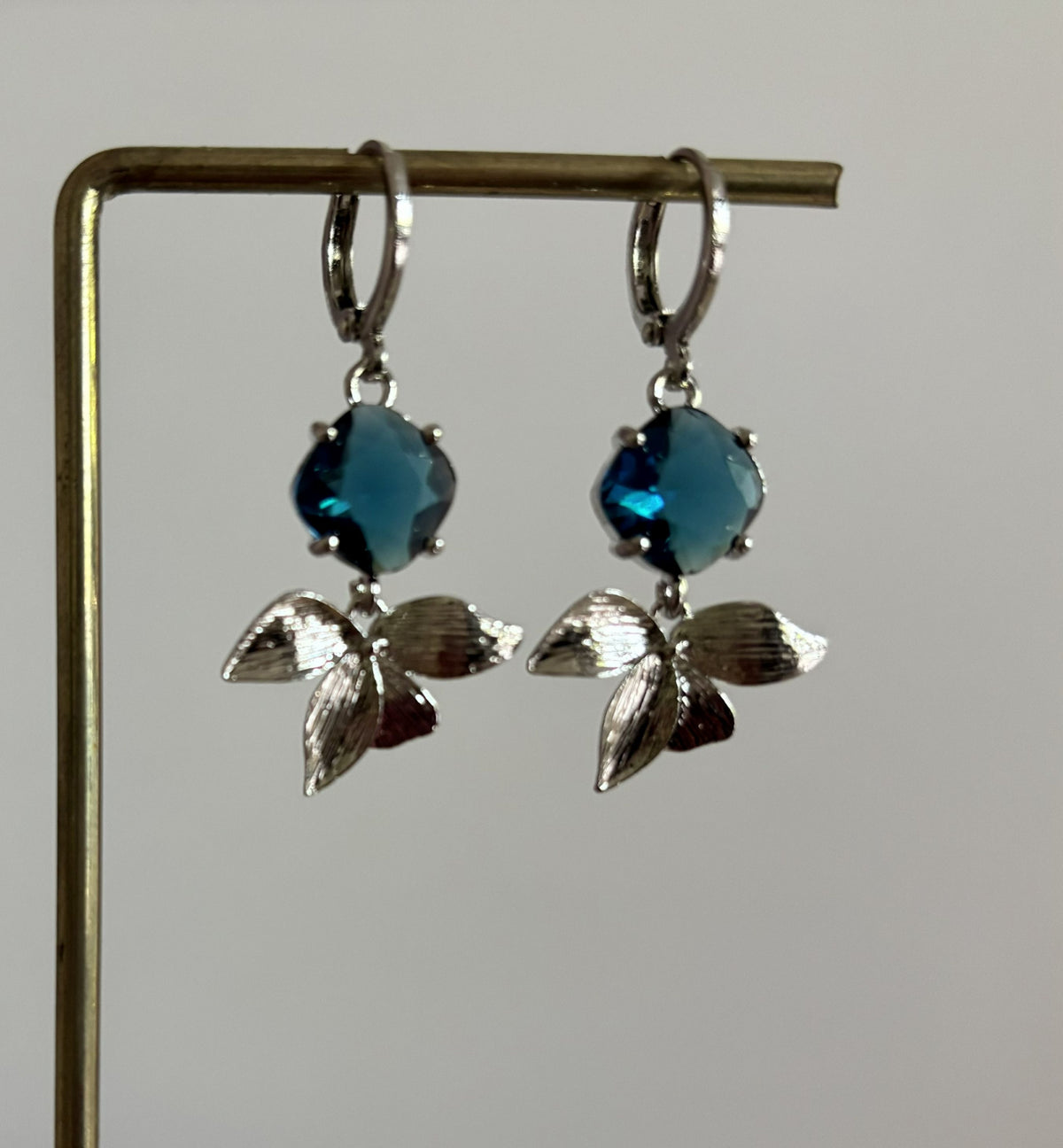 Zilverkleurige oorbellen Blossom bestaande uit ronde oorringen met hangende zilveren blaadjes en een diep blauwe glasbedel