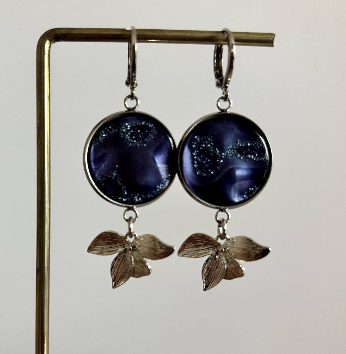 Zilverkleurige oorbellen Blossom bestaande uit ronde oorringen met hangende zilveren blaadjes en een diep blauw glitter cabochon