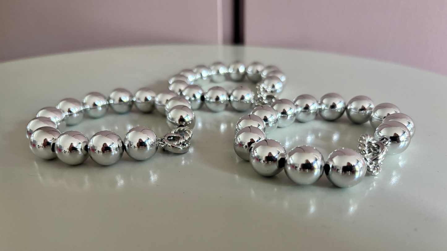 Drie zilverkleurige Bolletjesarmbanden Large met glanzende acryl kralen en een roestvrijstalen sluiting op een witte achtergrond.