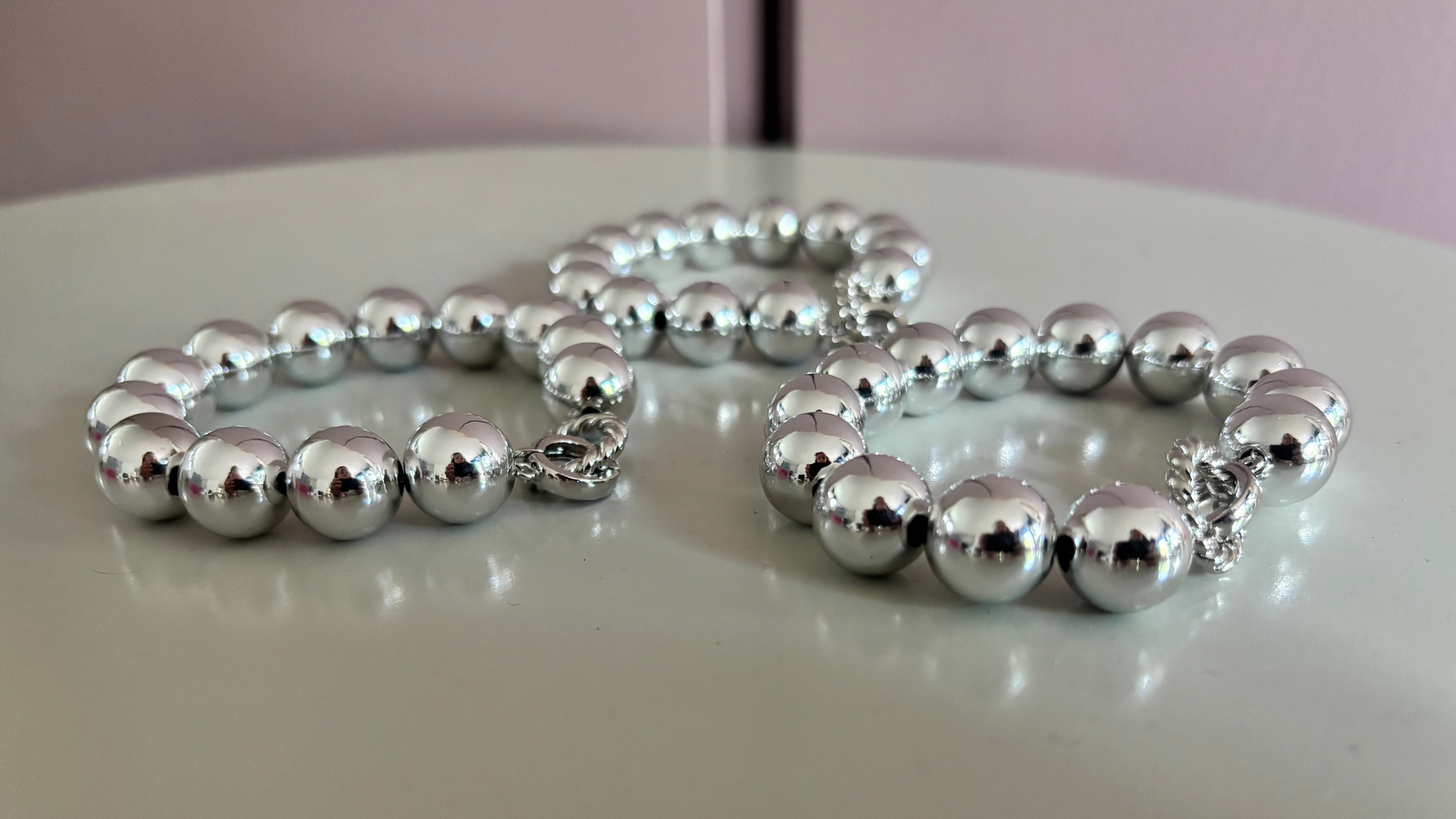 Drie zilverkleurige Bolletjesarmbanden Large met glanzende acryl kralen en een roestvrijstalen sluiting op een witte achtergrond.