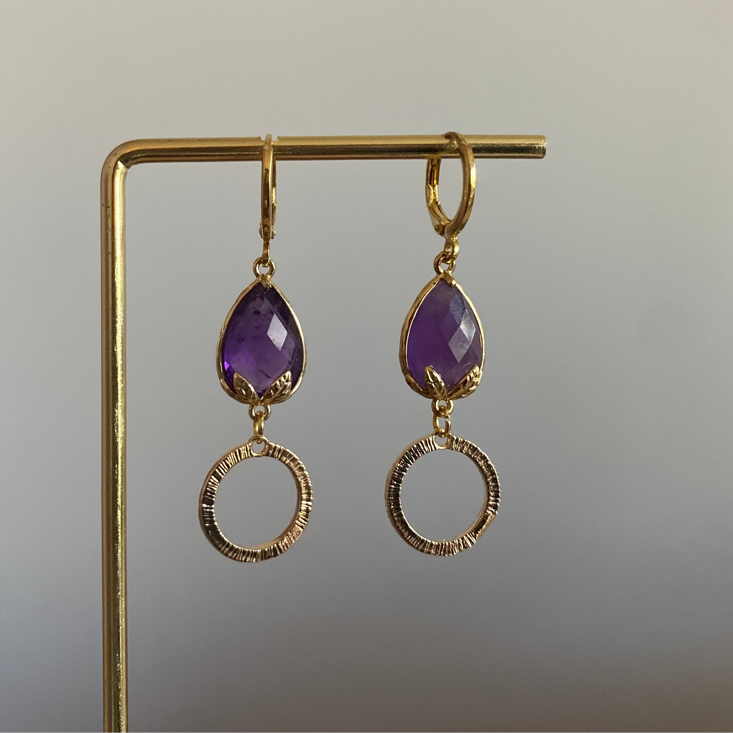 Korte oorbel met diep paarse peervormige steen met bladgoud en kleine gehamerde cirkel, circa 3 cm lang.