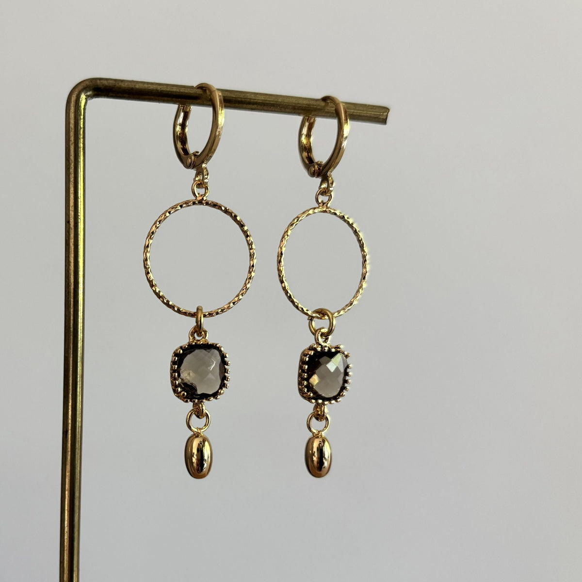 14k vergulde oorbellen Carien met een bewerkte ronde ring, vierkante gefacetteerde grijze kristalsteen en klein goud bedeltje.