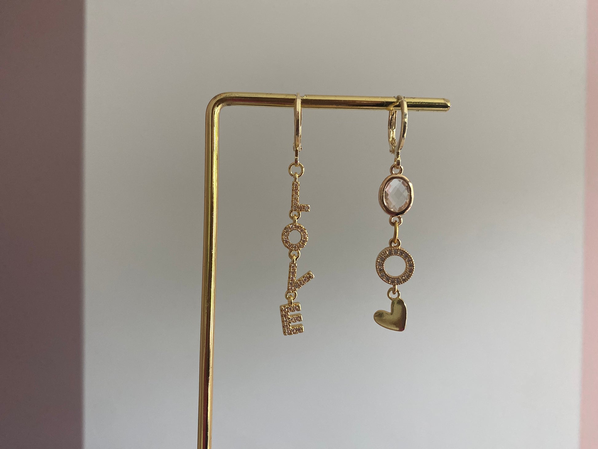 Asymmetrische oorbellen met links strass Love-hanger en rechts blanke glasbedel, zirkonia O en hartje, 14k verguld.