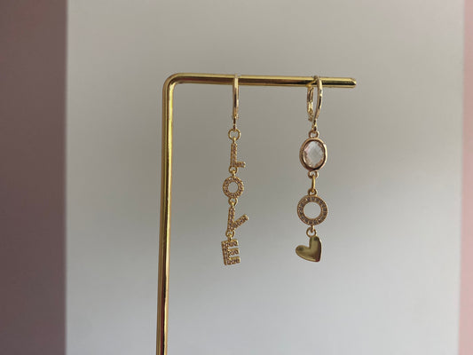 Asymmetrische oorbellen met links strass Love-hanger en rechts blanke glasbedel, zirkonia O en hartje, 14k verguld.