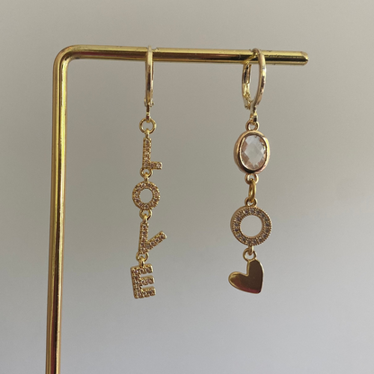 Asymmetrische oorbellen met links strass Love-hanger en rechts blanke glasbedel, zirkonia O en hartje, 14k verguld.