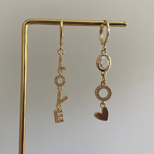 Asymmetrische oorbellen met links strass Love-hanger en rechts blanke glasbedel, zirkonia O en hartje, 14k verguld.