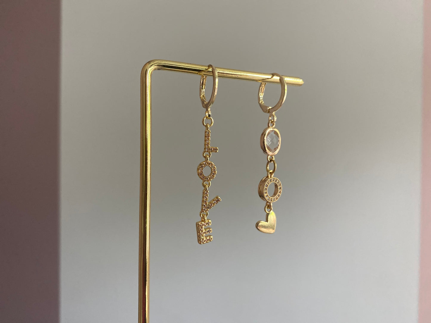 Asymmetrische oorbellen met links strass Love-hanger en rechts blanke glasbedel, zirkonia O en hartje, 14k verguld.