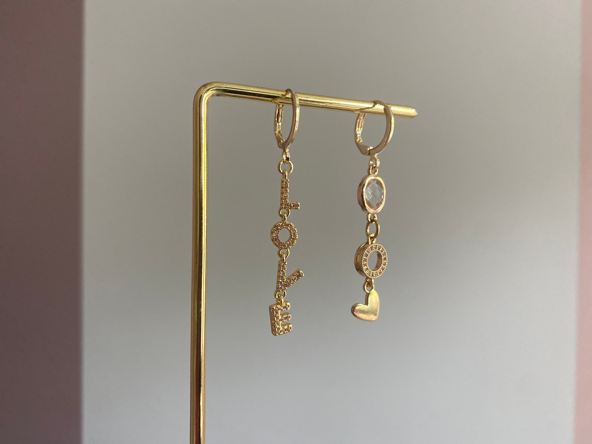 Asymmetrische oorbellen met links strass Love-hanger en rechts blanke glasbedel, zirkonia O en hartje, 14k verguld.