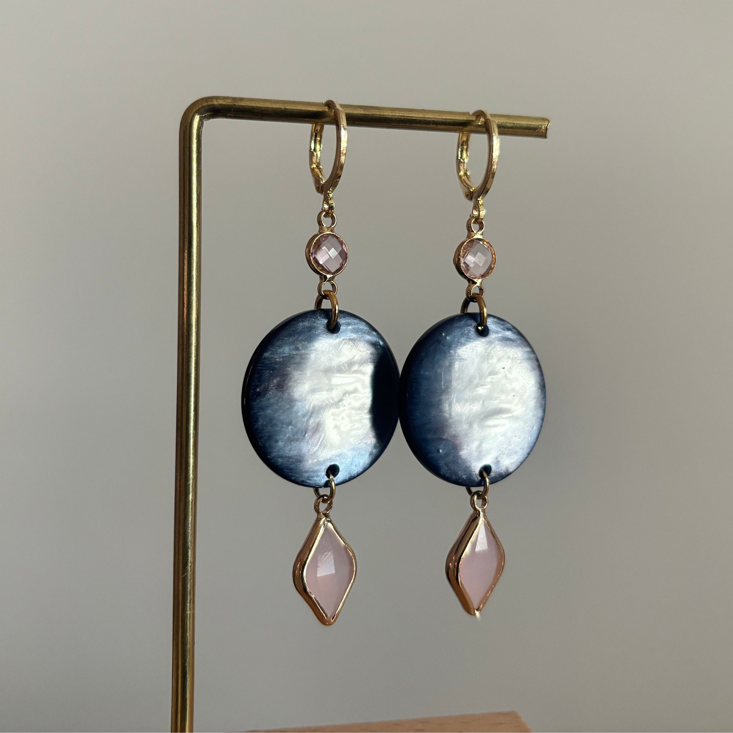 Lange gouden oorbellen bestaande uit een kleine ronde roze steen, een grote ronde donkerblauwe disc met parelmoerglans en onderaan een ruitvormige hanger in melkachtig roze.