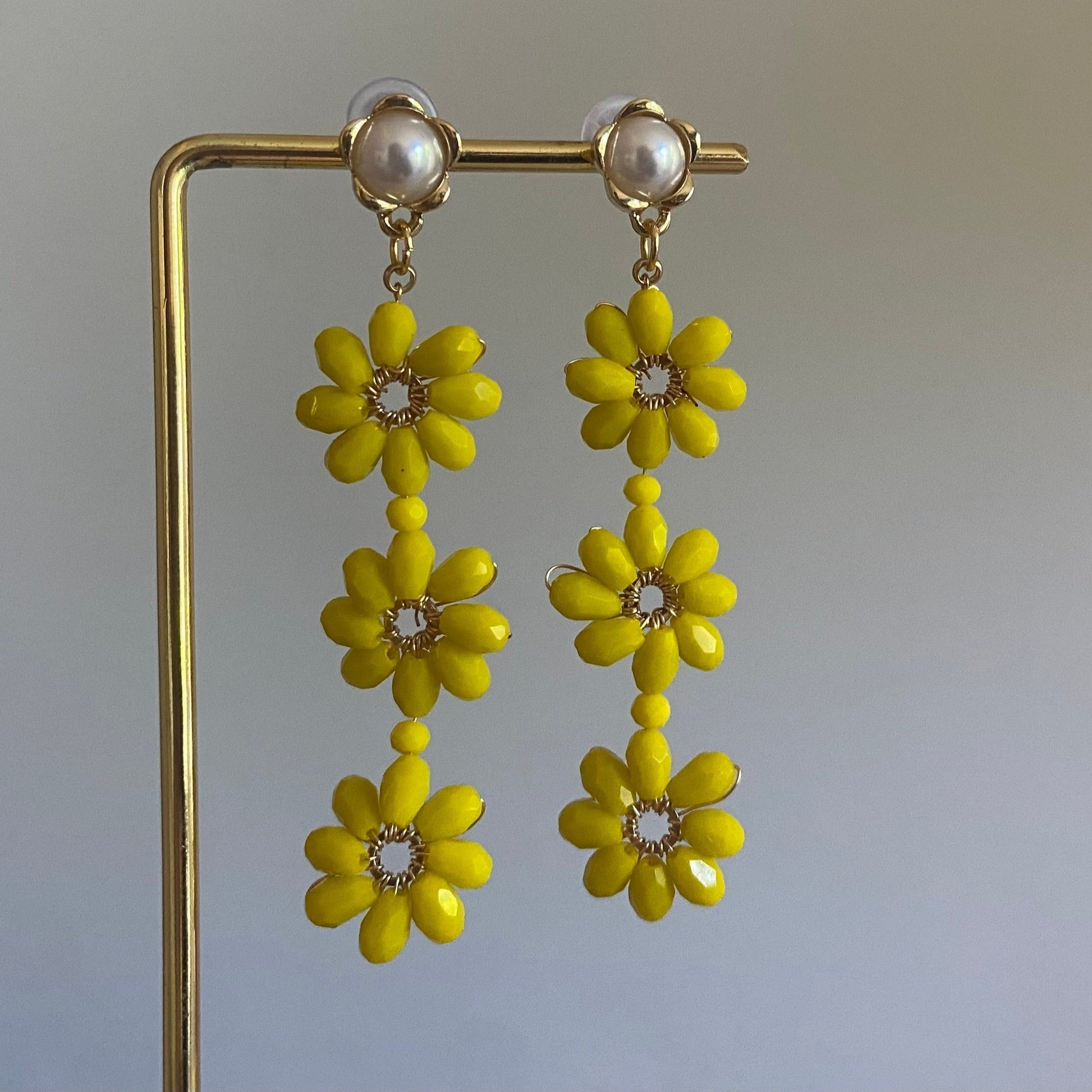 Handgemaakte oorbel met 3 gele  bloemen onder elkaar van glanzende kralen en een 14K vergulde steker met parel in de vorm van een bloem.