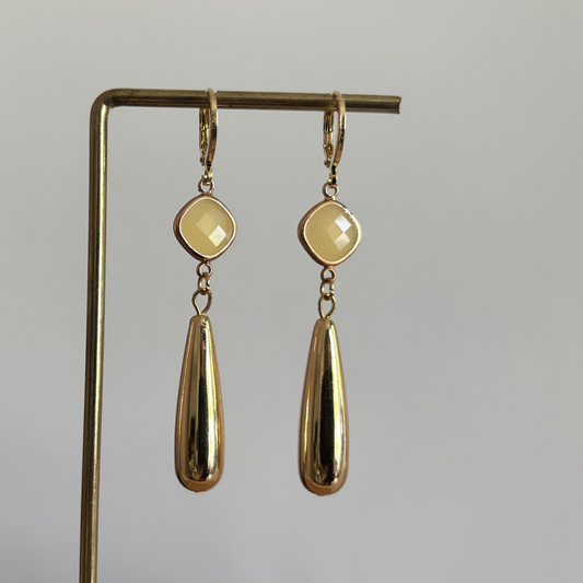 Gouden hanger oorbellen Ellen met matte gele jade-stenen en glanzende goudkleurige druppelhangers op een standaard.