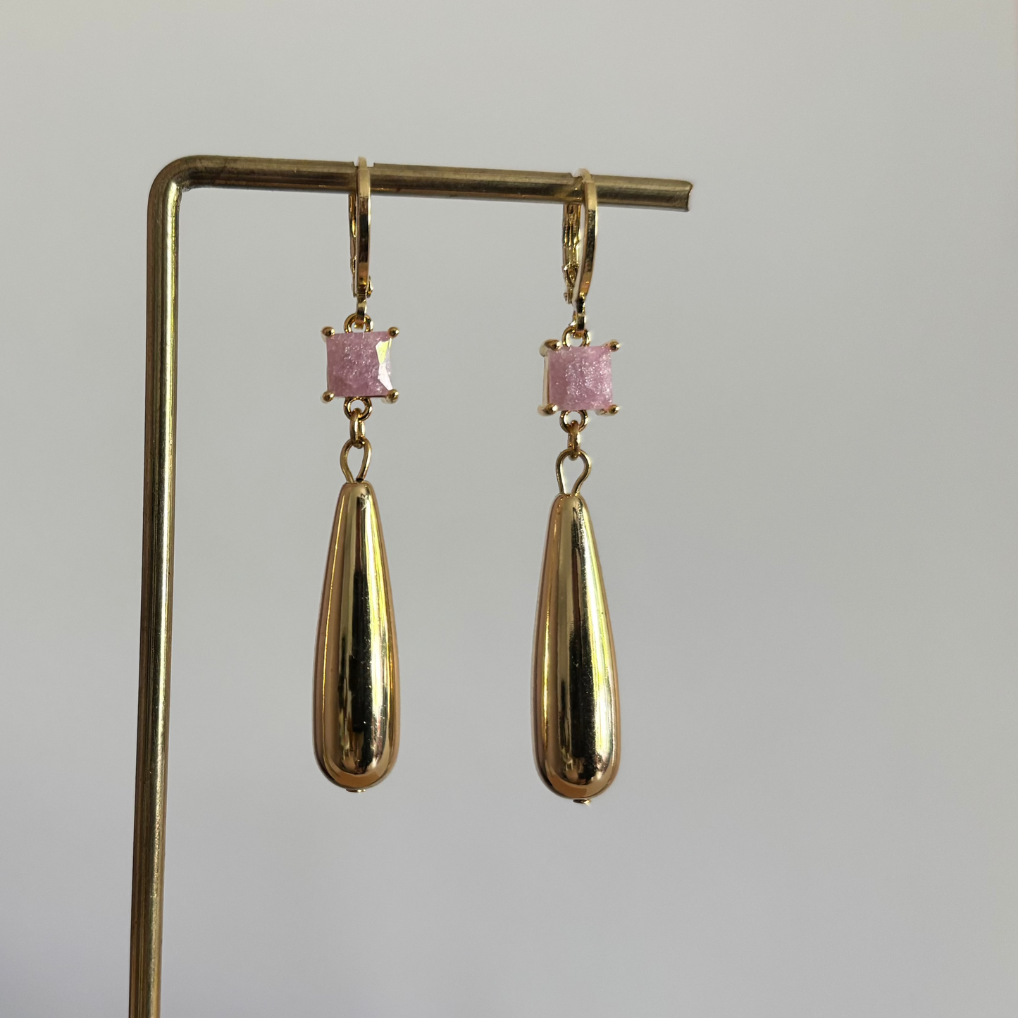 Gouden oorbellen Ellen met een mat roze vierkant steentje en een glanzende druppelhanger.