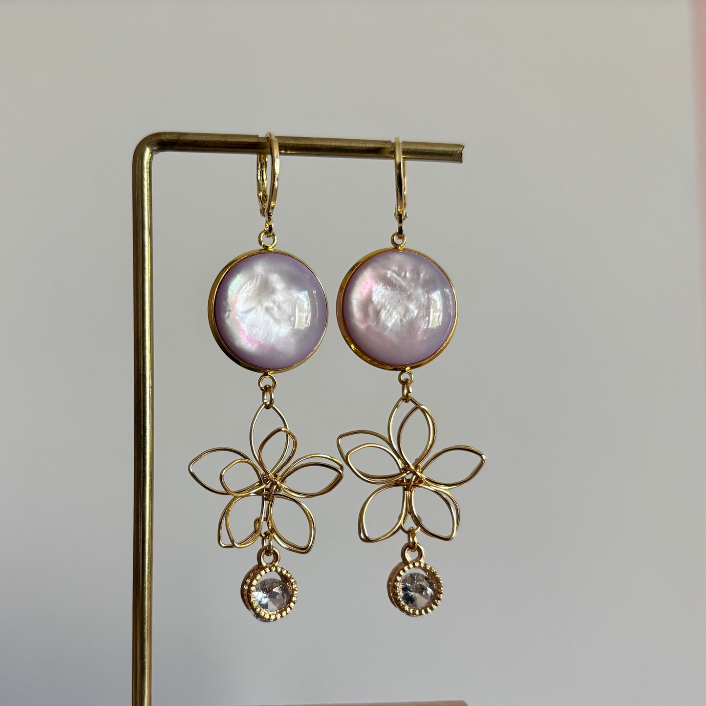 Symmetrische 14k gouden oorbellen met lila glitterstenen, zirkonia en gouden draadbedels in bloemvorm.