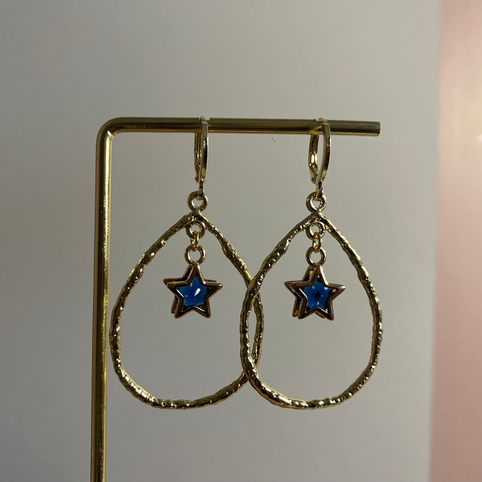 Een foto van de Estelle oorbellen van lellebel sieraden. 14k vergulde oorbel met ster en steentje in open ring, feestelijke lengte van 4 cm.