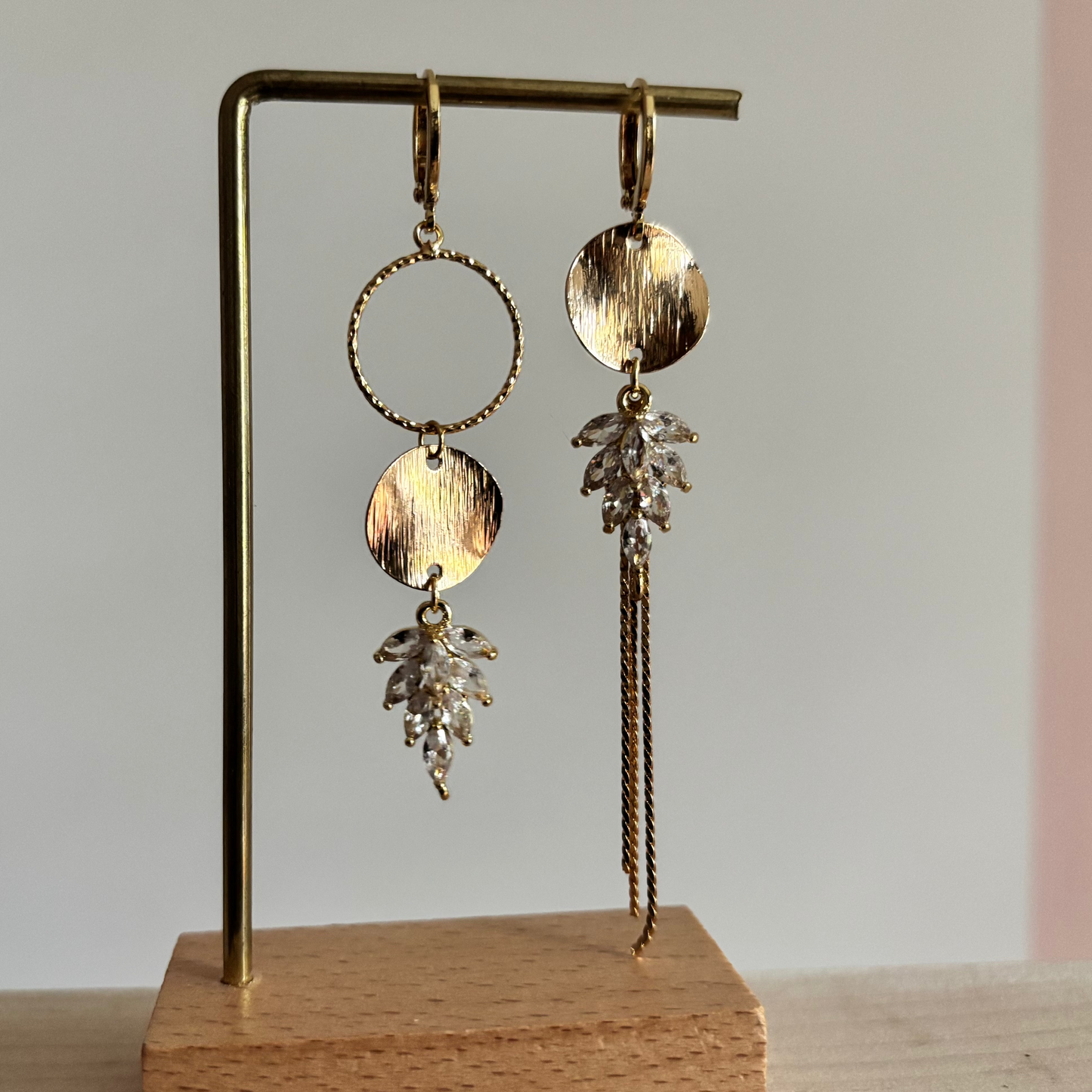 Gouden asymmetrische oorbellen Fabienne met schwarze steentjes op een standaard.