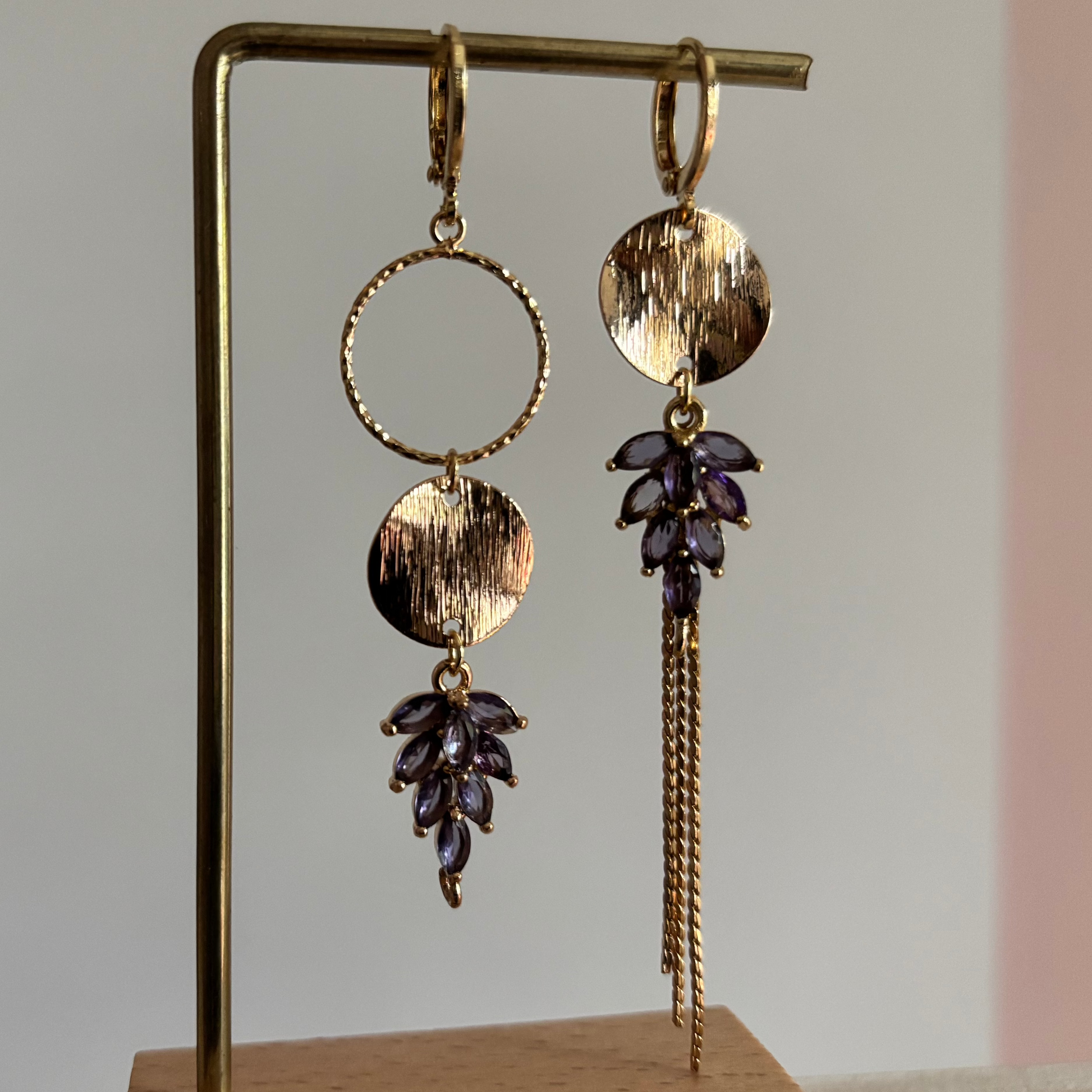 Gouden asymmetrische oorbellen Fabienne met schwarze steentjes op een standaard.