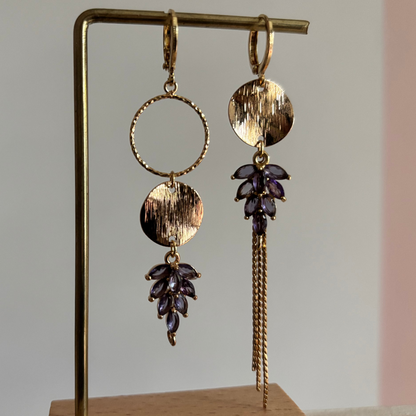 Gouden asymmetrische oorbellen Fabienne met schwarze steentjes op een standaard.