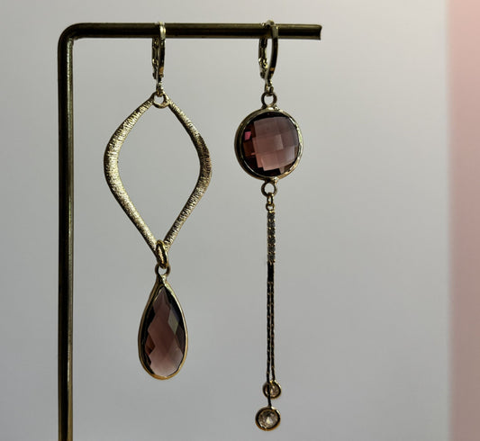 Goudkleurige asymmetrische oorbellen Floor Bordeaux met een grote open ruit met bordeauxrode druppel en een strakke hanger met schijfje en zirkonia.