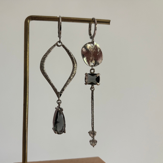 Zilverkleurige asymmetrische oorbellen Floor Zilver met een grote open ruit met grijze druppel en een strakke hanger met schijfje en zirkonia.