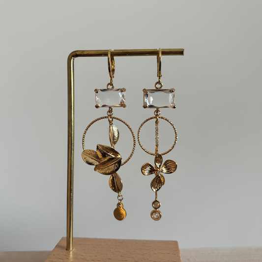 Asymmetrische 14K vergulde oorbellen met glazen bedels en gouden bloem- en bladmotieven.