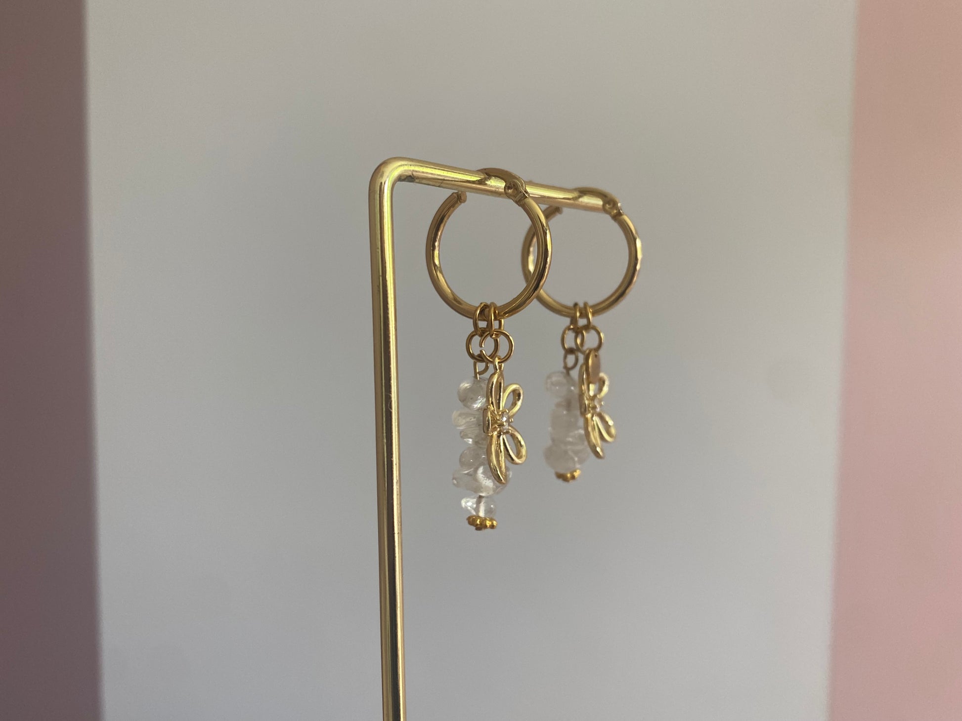 foto van de zijkant van andgemaakte vergulde gouden oorbellen bestaande uit RVS hoops met daaraan witte en zachtroze natuurstenen met een 14K vergulde bloembedel met ingelegde zirkonia.